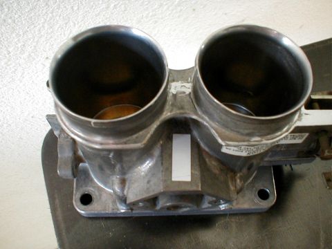 1996 Ford Bronco - A close-up view of a dual throttle body, a component of an engine's air intake system.