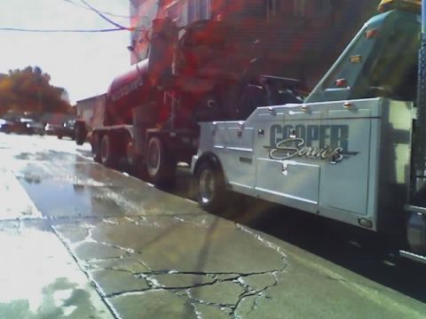 1992 Ford Bronco - A tow truck is seen with a cement mixer truck attached to it on a wet street.
