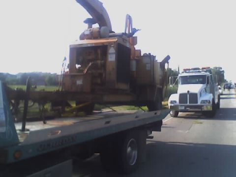 1992 Ford Bronco - A tow truck transports a large industrial wood chipper down a highway, with other vehicles in the distance.