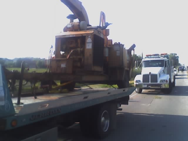 Tow truck carrying a large wood chipper on the highway, with another truck visible ahead