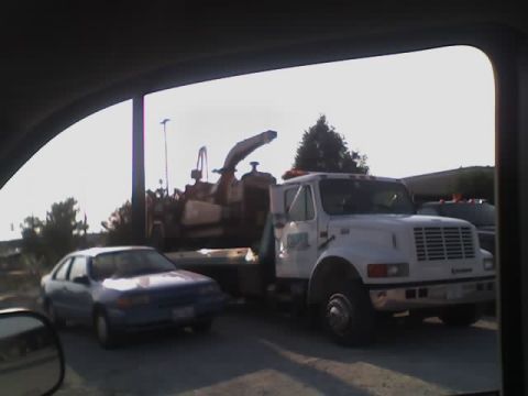 1992 Ford Bronco - A blue sedan is parked next to a white International truck equipped with a wood chipper.