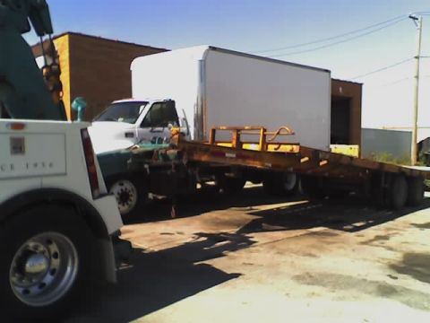 1992 Ford Bronco - A tow truck is connected to a trailer carrying a white box truck.