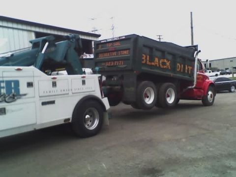 1992 Ford Bronco - A tow truck is connected to a dump truck, preparing to move it. The dump truck has "BLACK DIRT" written on its side.