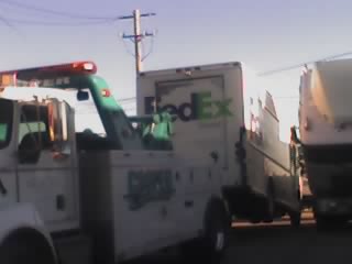 1992 Ford Bronco - A tow truck is parked next to a white FedEx truck under a utility pole.