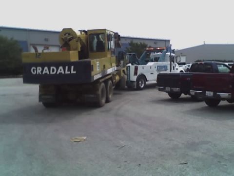 1992 Ford Bronco - A yellow Gradall machine is seen on a truck chassis, with a white tow truck and red pickup trucks in the background.