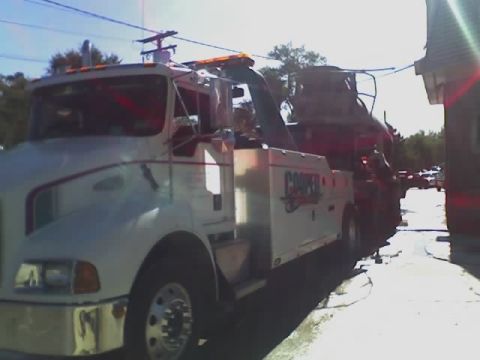 1992 Ford Bronco - A tow truck is transporting a vehicle down a street. The tow truck has 'COOPER' written on its side.