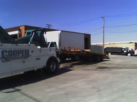 1992 Ford Bronco - A tow truck is positioned next to a flatbed trailer, with another truck visible in the background.