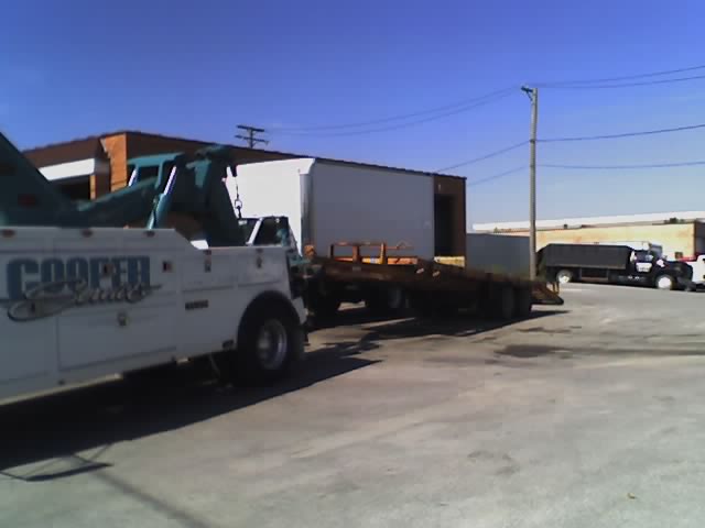 tow truck with 'COOPER' text, towing a flatbed trailer. Another truck is parked nearby