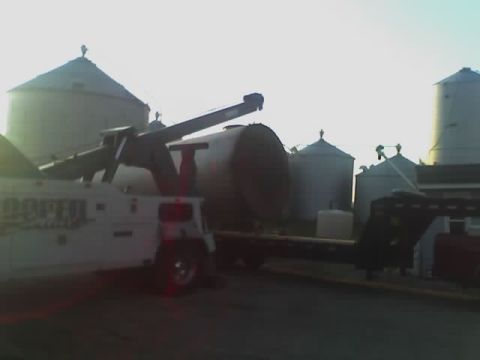 1992 Ford Bronco - A tow truck is seen from the side, hauling a trailer with a large tank inoperable tank.