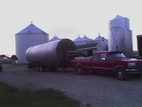 1992 Ford Bronco - A red pickup truck tows a large cylindrical trailer past farm silos.