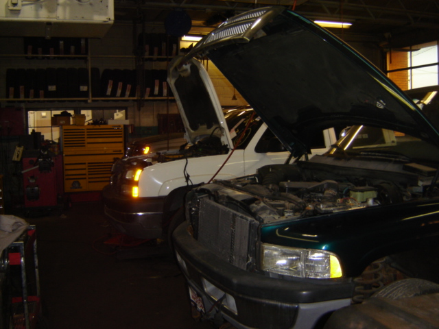 Green truck in foreground with hood open, white truck behind it with hood open