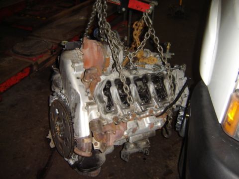 1992 Ford Bronco - Engine assembly is suspended by chains in a workshop environment, with a portion of a white vehicle visible.