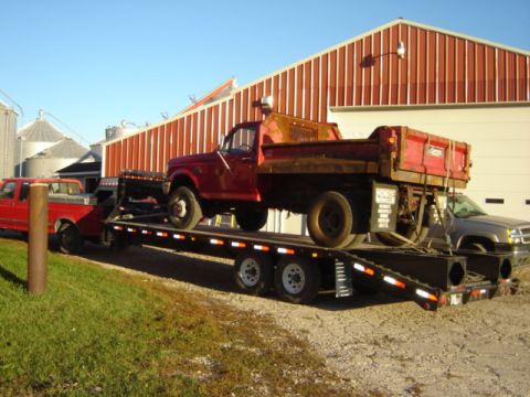 1992 Ford Bronco - A red dump truck is being transported on a flatbed trailer, pulled by a red pickup truck.