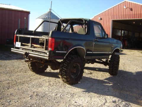 1992 Ford Bronco - Modified 1992 Ford Bronco with off-road tires sits in a gravel lot near a red barn.