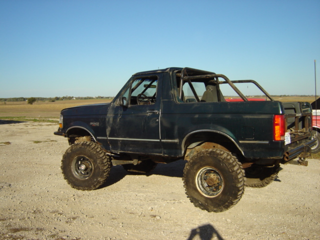 Dark green 1992 Ford Bronco with off-road tires and roll cage, side view