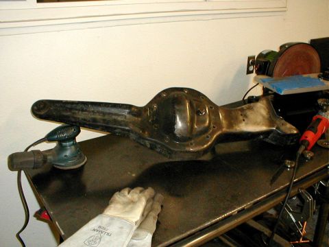 1996 Ford Bronco - A bare rear axle housing sits on a steel welding bench, its center pumpkin and tubes stripped and partly sanded to bright metal. A green ra…