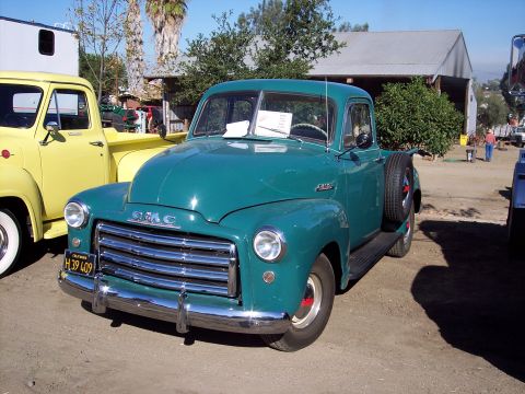 1981 Kenworth W900A - A vintage teal GMC pickup truck is parked next to a yellow truck at an outdoor event.