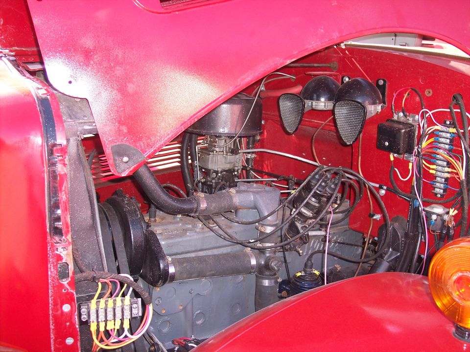 Red engine bay with visible engine block, carburetor, wiring, and dual horns