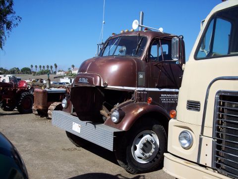 1981 Kenworth W900A - A brown GMC truck is parked next to a cream-colored truck under a clear blue sky.