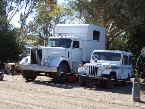 1981 Kenworth W900A - A white semi-truck with a camper shell is parked next to a white jeep, with trees and a small tractor in the background.