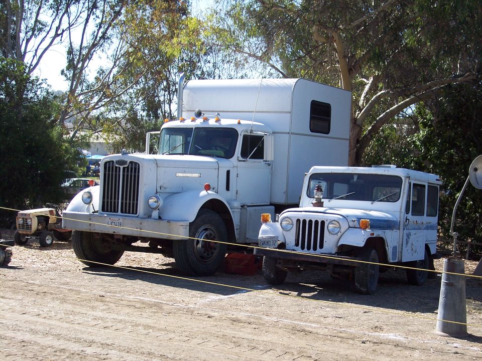 Weathered white bullnose conventional semi tractor with sleeper parked beside white Jeep van