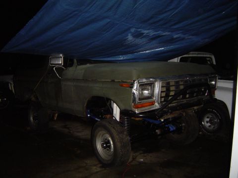 1978 Ford Bronco - Customized pickup truck with lifted suspension and aftermarket bumper, parked under a tarp next to another vehicle.