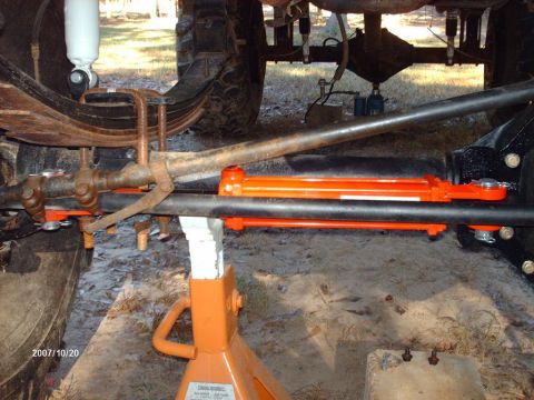 1990 Ford F-150 - Vehicle steering linkage and suspension parts are shown on jack stands, with an orange hydraulic assist cylinder installed.