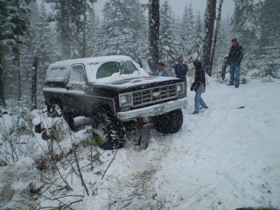 Black lifted Chevrolet Blazer in deep snow in a forest during snowfall