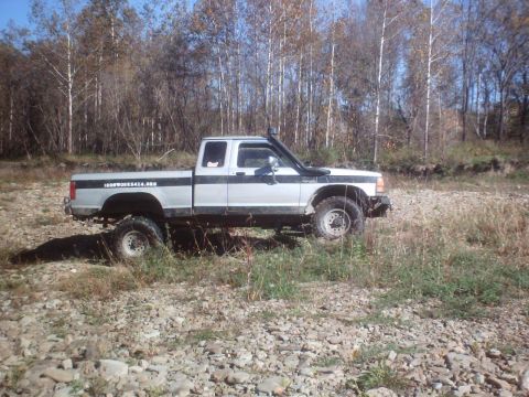 1990 Ford Ranger - A lifted pickup truck with a snorkel is parked on a rocky, dry creek bed with trees in the background.