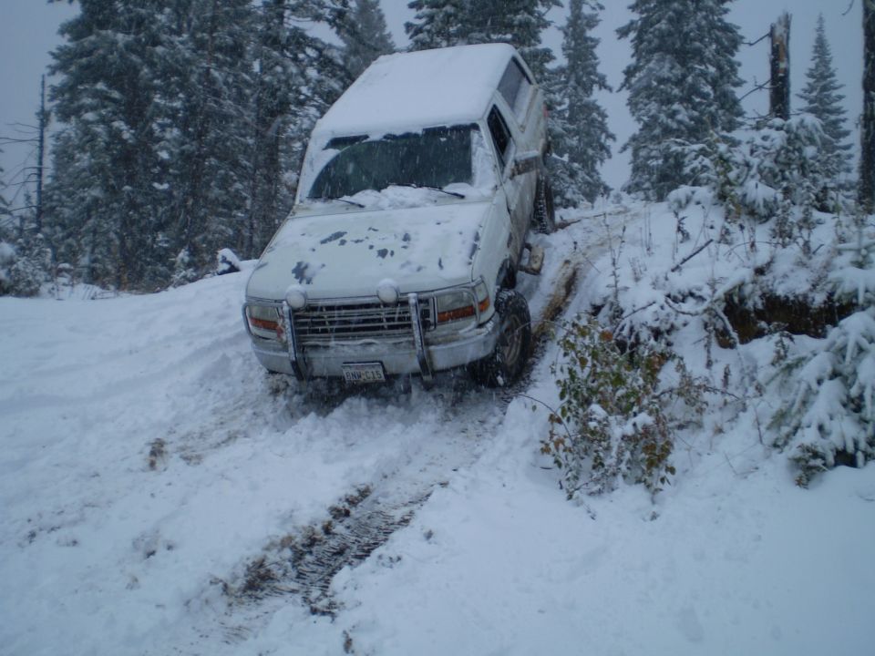 White 1992 Ford Bronco with aftermarket bumper stuck in snow on a wooded trail