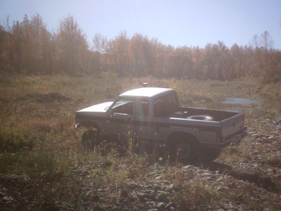1990 Ford Ranger pickup truck, lifted, in a grassy field with trees