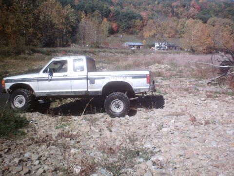 1990 Ford Ranger - Lifted 1990 Ford Ranger parked on a rocky incline with autumn foliage in the background.