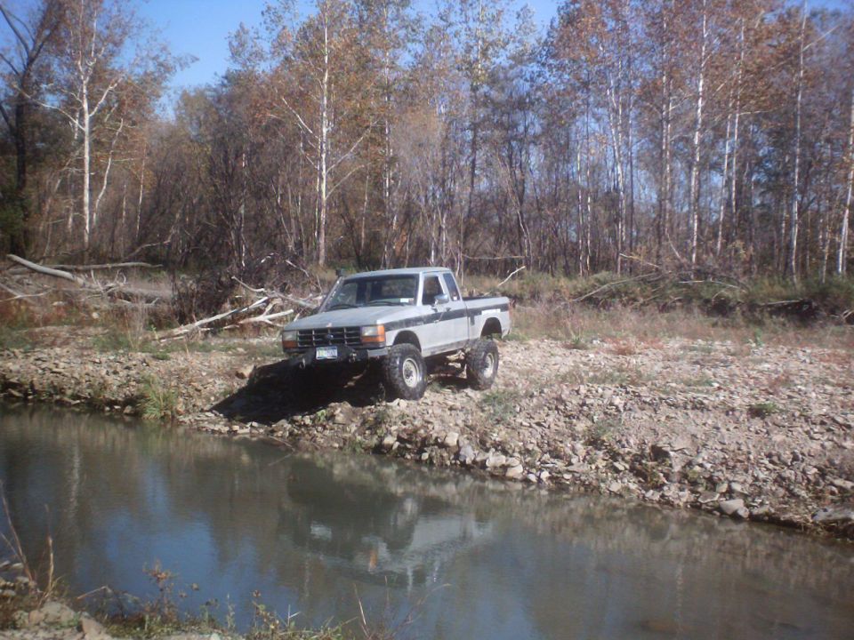 Lifted pickup truck parked by a stream with trees in the background
