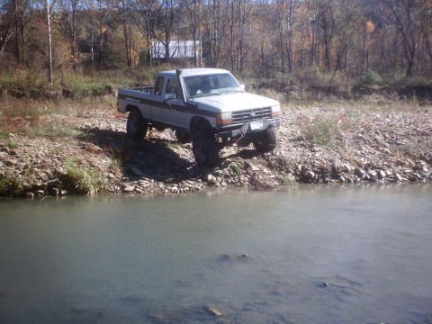 1990 Ford Ranger - A lifted 1990 Ford Ranger pickup truck is parked on the rocky shore of a body of water.