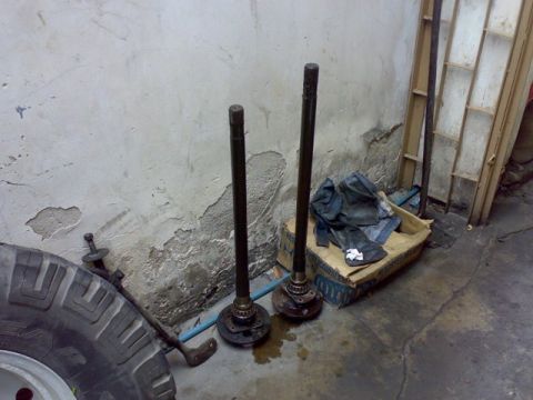1995 Ford F-150 - Two axle shafts and a tire are shown in front of a concrete wall, with a box of items in the background.