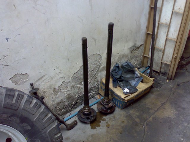 Two axle shafts and a tire leaning against a wall. A cardboard box with some clothes is nearby
