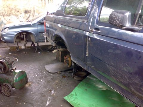 1995 Ford F-150 - A dark blue pickup truck is undergoing repairs in a garage, with its rear axle removed.
