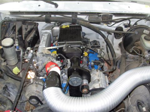 1994 Ford Bronco - The engine bay of a 1994 Ford Bronco shows a large silver intake pipe and various blue-colored engine components.