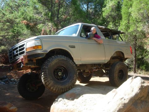 1995 Ford Bronco - Modified 1995 Ford Bronco tackling an off-road trail with large tires and lifted suspension.