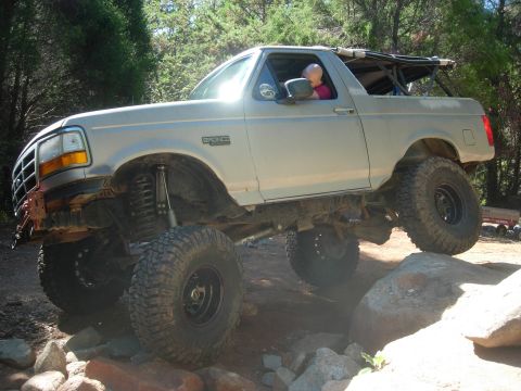 1995 Ford Bronco - This modified 1995 Ford Bronco navigates a rocky off-road path with its suspension articulation clearly visible.