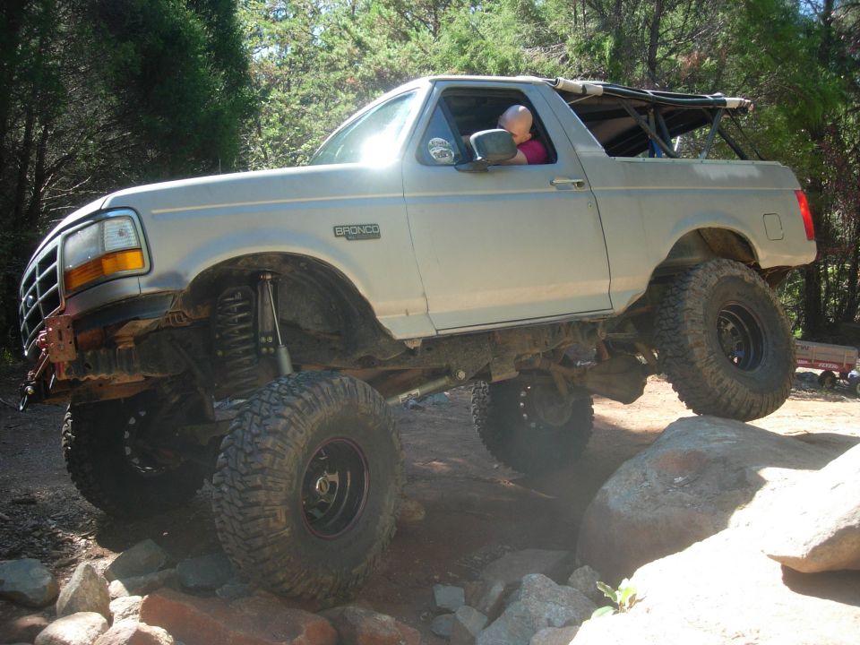 Lifted 1995 Ford Bronco driving over rocks on a trail