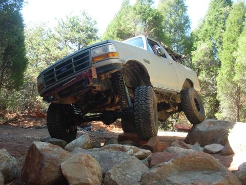 1995 Ford Bronco - A modified Ford Bronco tackles a challenging off-road course with its tires on large rocks.