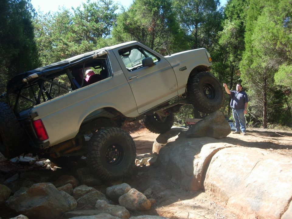 Tan Ford Bronco off-roading over rocks, with a man standing nearby