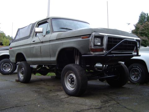 1978 Ford Bronco - This lifted SUV has a custom front bumper and a soft top, parked next to another vehicle.