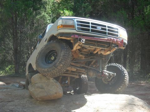 1995 Ford Bronco - This modified Ford Bronco is navigating a challenging off-road obstacle, with one wheel significantly elevated.
