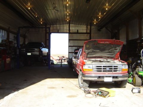 1992 Ford Bronco - A red pickup truck with its hood open is parked in a garage, with another vehicle on a lift in the background.