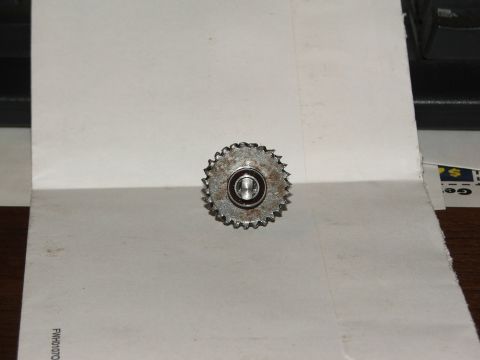 1996 Ford Bronco - A small toothed steel sprocket or idler gear with a sealed bearing pressed into its center, laid on a sheet of white paper on a wooden desk…