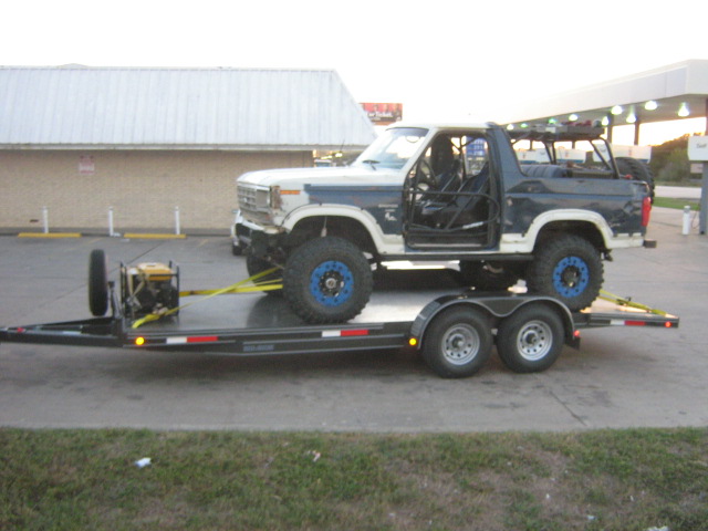 Modified Ford Bronco on a dual-axle trailer, with roll cage visible inside