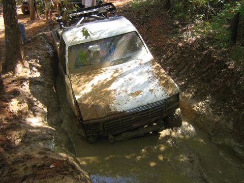 1986 Ford Bronco - An off-road truck navigates a challenging muddy terrain, with onlookers present.