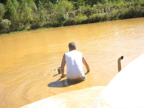1986 Ford Bronco - A person is partially submerged in murky water next to a vehicle's exhaust pipe.